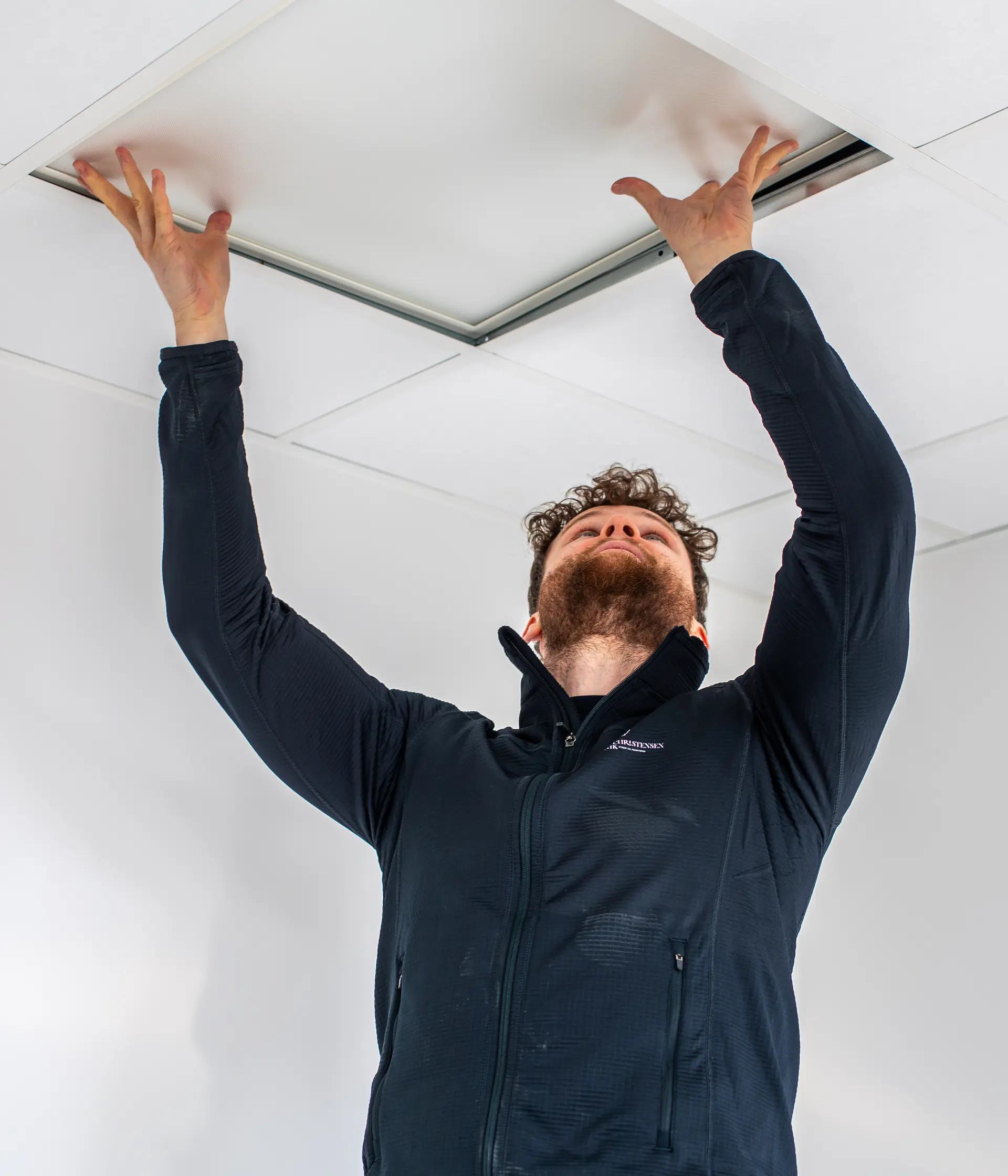 Elektriker monterer loftpanel med armene op, fysisk håndværk